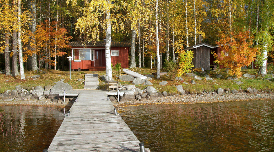 Un chalet au bord d’un lac pendant que les arbres changent de couleur, illustrant comment hiverniser votre chalet.
