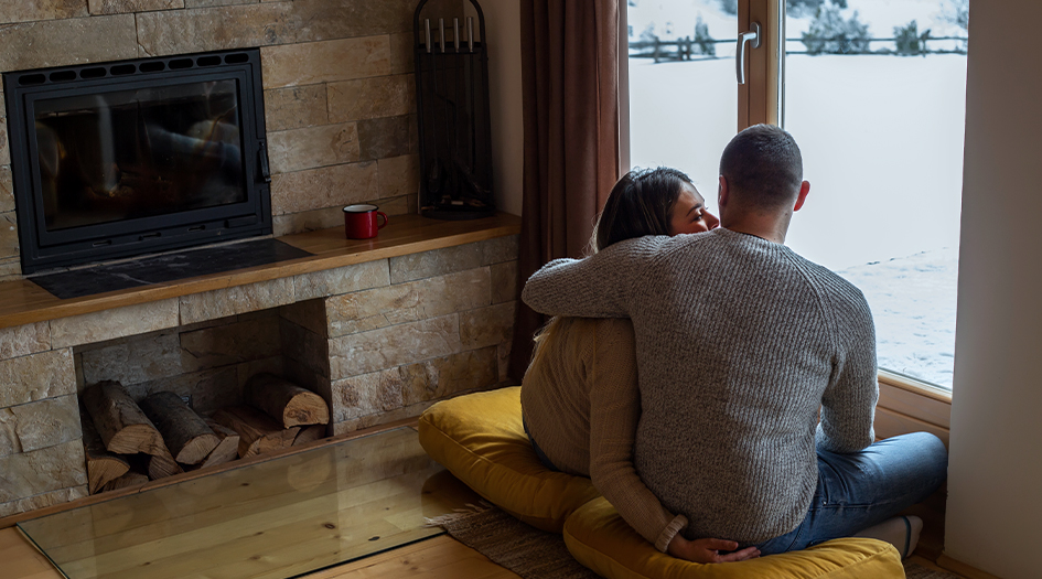 A couple sits at a window looking at the snow, showing how you can winterize your cottage and turn it into a four-season home