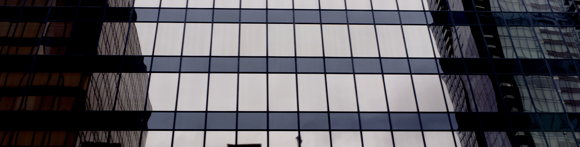Gros plan sur la façade vitrée d'un immeuble de bureaux moderne, où se reflètent le ciel et les bâtiments environnants.