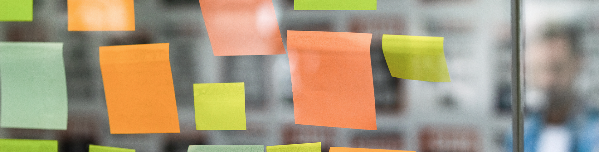 A close-up of colourful sticky notes on a glass wall during a brainstorming session.