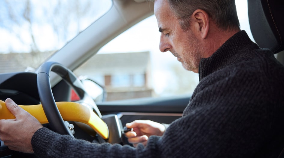 A man places a yellow steering wheel lock on his car, to help protect his vehicle with an aftermarket anti-theft device.