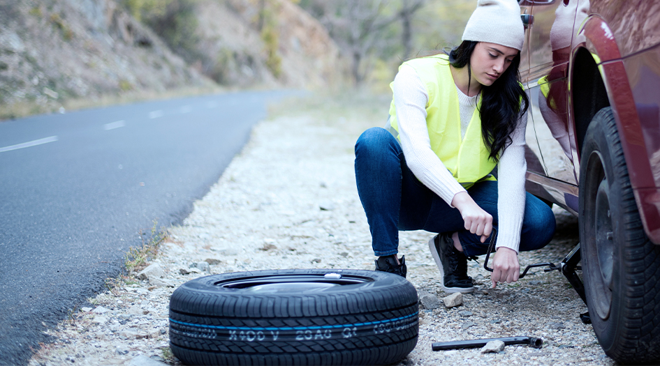 A woman puts a jack under her car, showing you how to change a tire