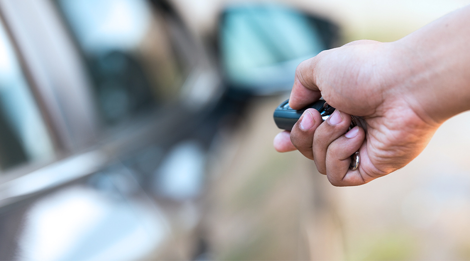 A close up on a hand pressing the lock button on a key fob shows one way to prevent car theft