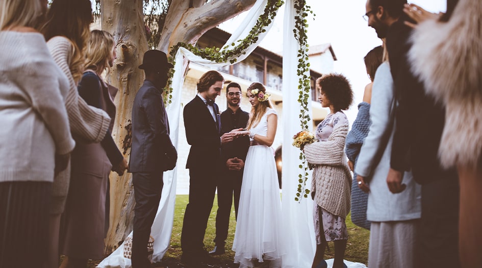 A couple gets married outside surrounded by their guests, showing how you can insure your backyard wedding