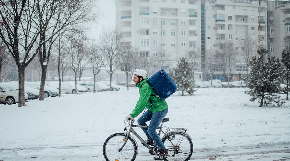 A man rides a bicycle in the snow, following the guide to safe winter biking