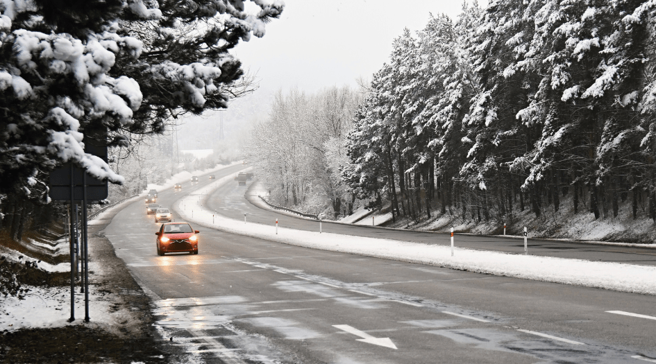 A line of cars drives down a snowy forest road, showing one area where black ice is likely to form.