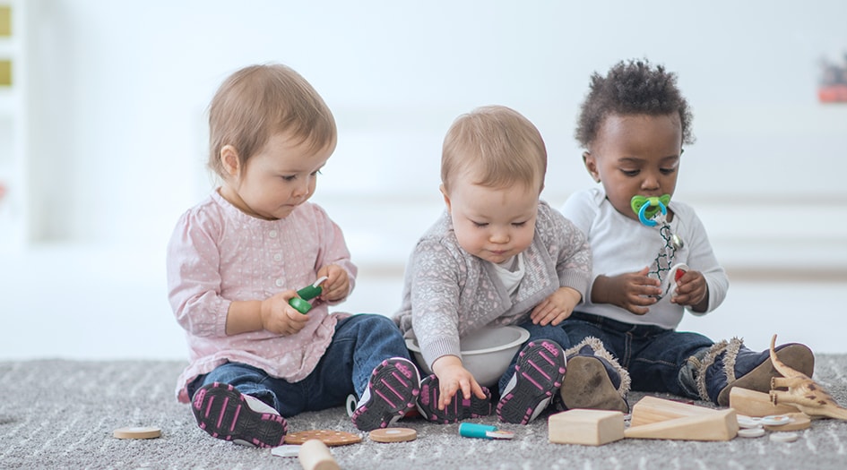 There are different insurance policies one should consider before opening a home daycare, as shown by three small children playing on the floor