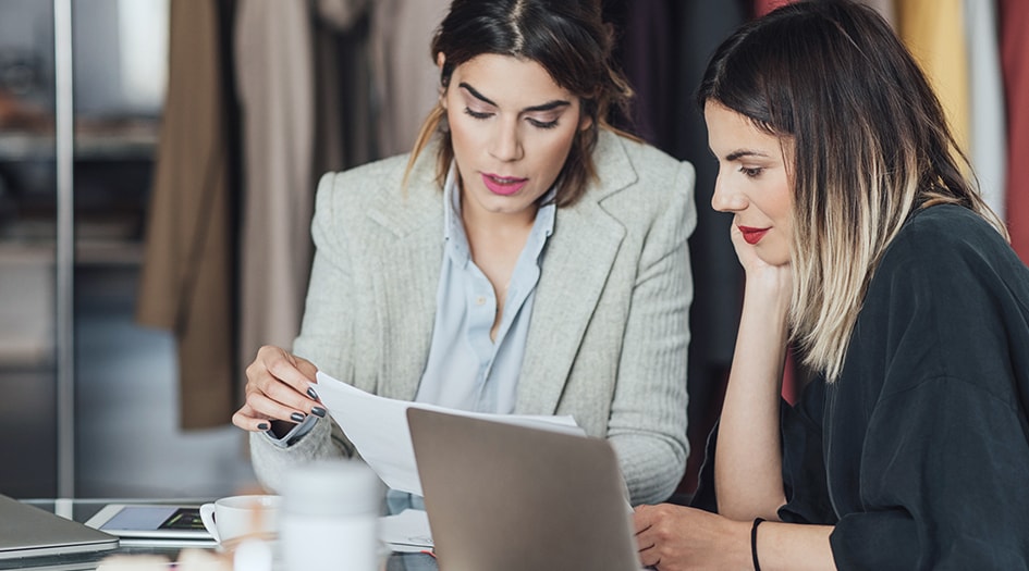 Two women sit at a laptop reviewing paperwork, showing the difference between an insurance broker and agent
