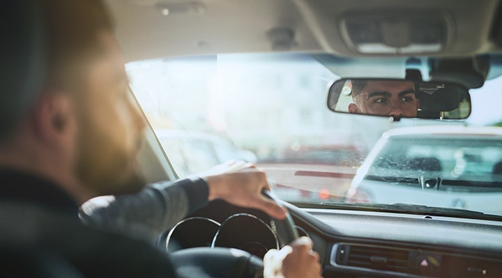 Navigating blind spots can be difficult, so always check your mirrors, as shown by a man sitting in his car looking in his rearview mirror