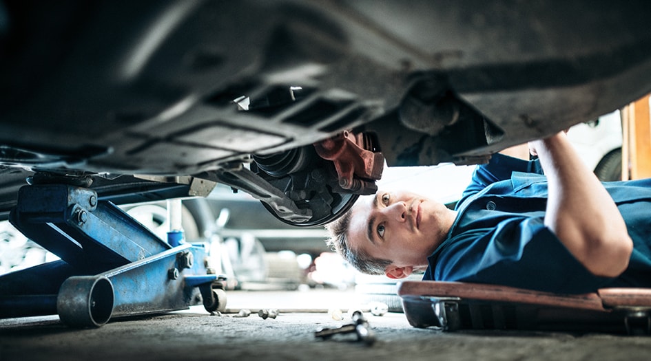 A mechanic is inspecting under a car, showcasing whether you need to get your car repaired after a collision 