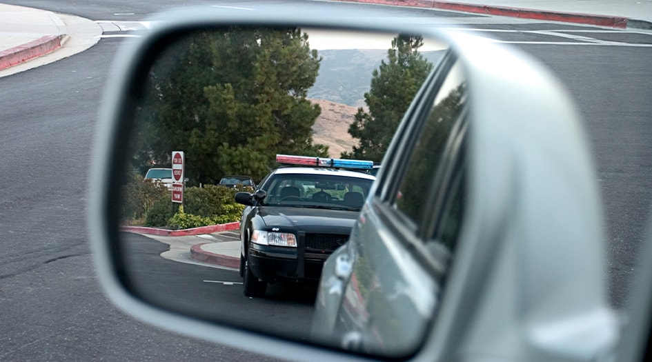 A close up shows a cop car in a vehicle's side mirror, showing you what you need to know about out-of-province traffic tickets