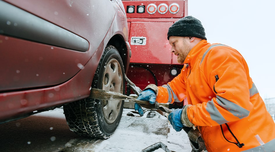A man hooks up a car's tire to a tow truck, showing what to do before you have your vehicle towed