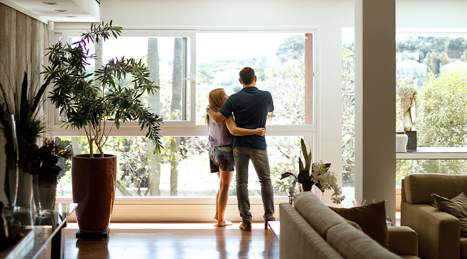 A man and woman look out the window of their living room, showing simple ways to avoid common home insurance claims