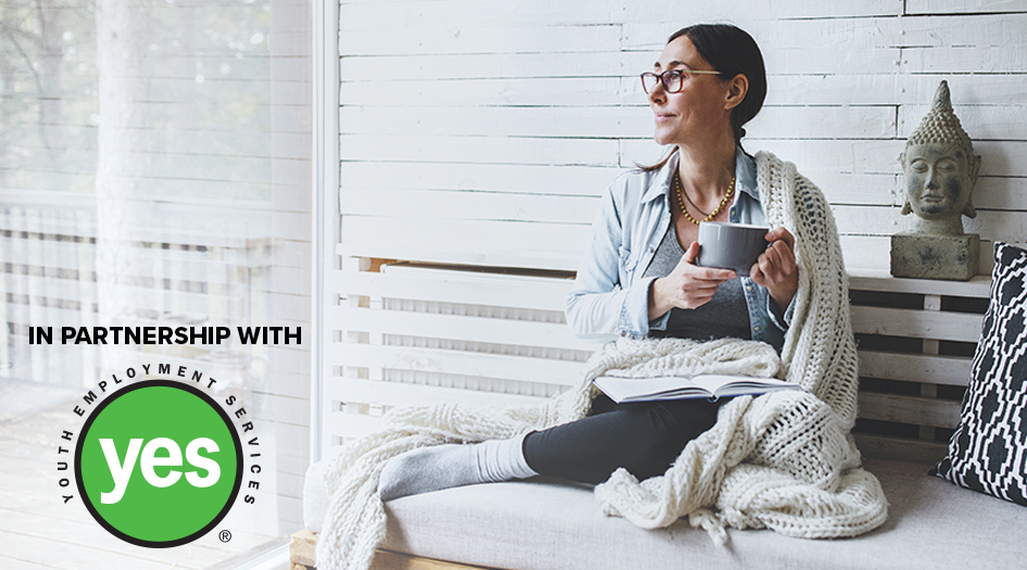 A woman smiles and sits on a couch with a mug, showing you how to take care of your mental health through COVID-19 and beyond - In partnership with Youth Employment Services (YES)