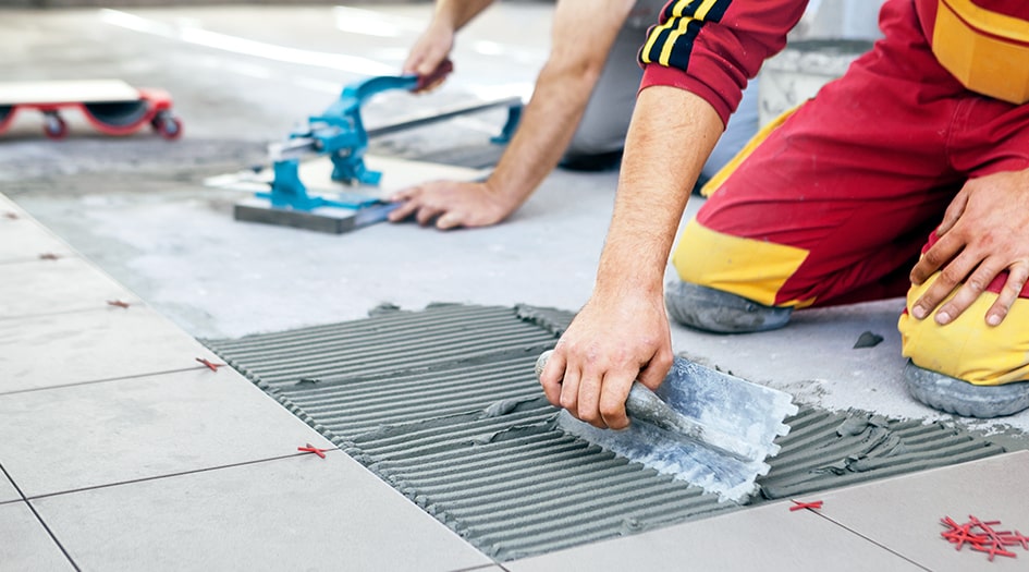 Two individuals spread grout while tiling a floor, avoiding the 7 home renovation mistakes