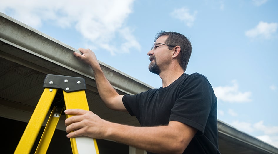 A man checks his roof on a ladder, showing how to keep your roof in tip-top shape