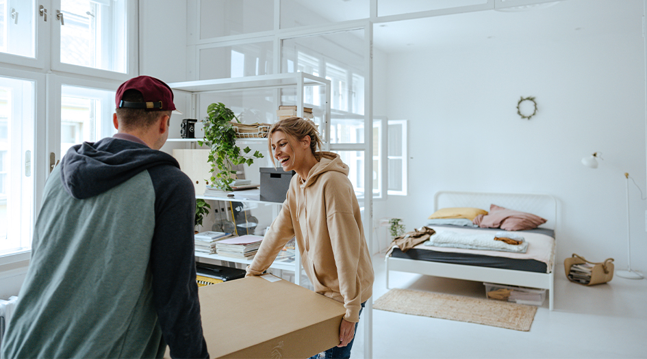 A man and woman move a large box into an apartment, as they wonder if subletting their rental space will affect tenant insurance