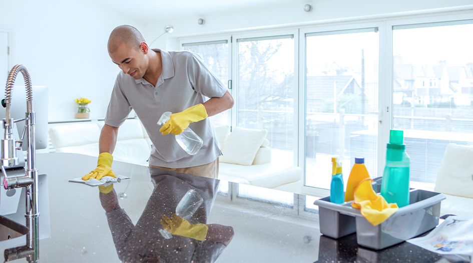 Here's what the hazard symbols mean on cleaning products, as shown by a man spraying cleaner on a kitchen counter