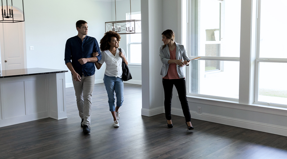 A couple walks through an empty apartment with a real estate agent, as she explains whether they need home insurance to get a mortgage