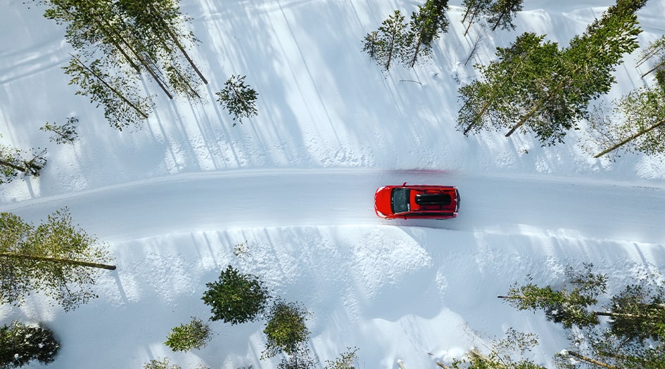 A red car drives along a plowed path in the snowy forest, showing one way to drive safely in the snow.
