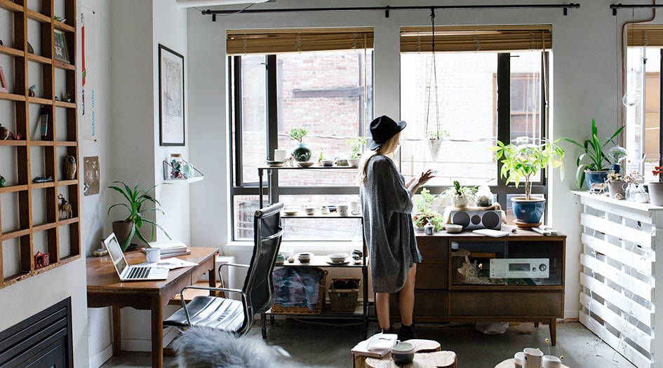 A young woman stands in an open-concept apartment, reading how much tenant insurance costs on her tablet