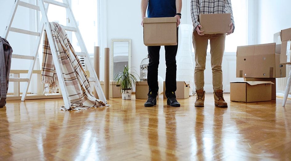 Two men hold cardboard boxes in a room of household items that tenant insurance can help protect in the event of an emergency