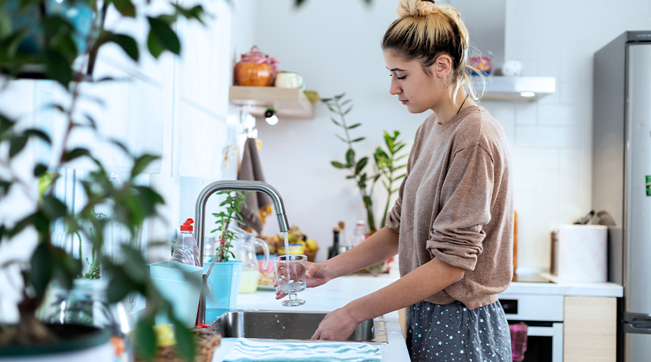 A woman fills up a glass with water at her kitchen sink, showing how you can prevent water damage as a tenant