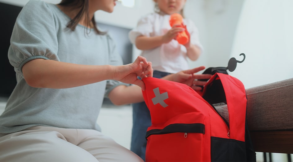 A woman packs a red first aid backpack, showing one way to prepare for a natural disaster