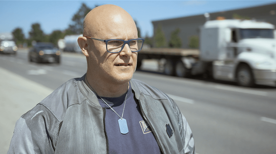 Don stands safely on the side of the road, explaining how his insurance claim restored his motorcycle after an accident.