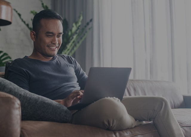 Person sitting on their couch while doing work on thier laptop computer