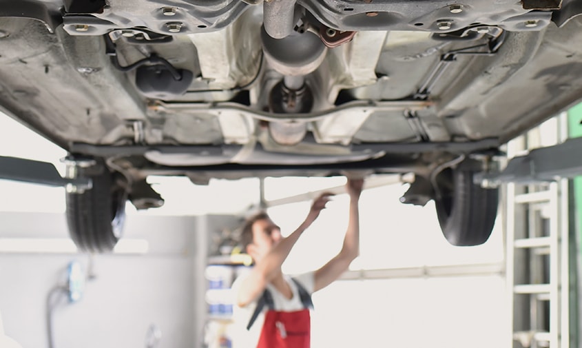 A qualified mechanic and customer standing beside a car on a hoist
