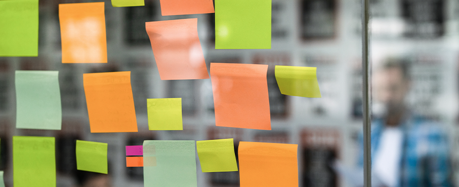 A close-up of colourful sticky notes on a glass wall during a brainstorming session.