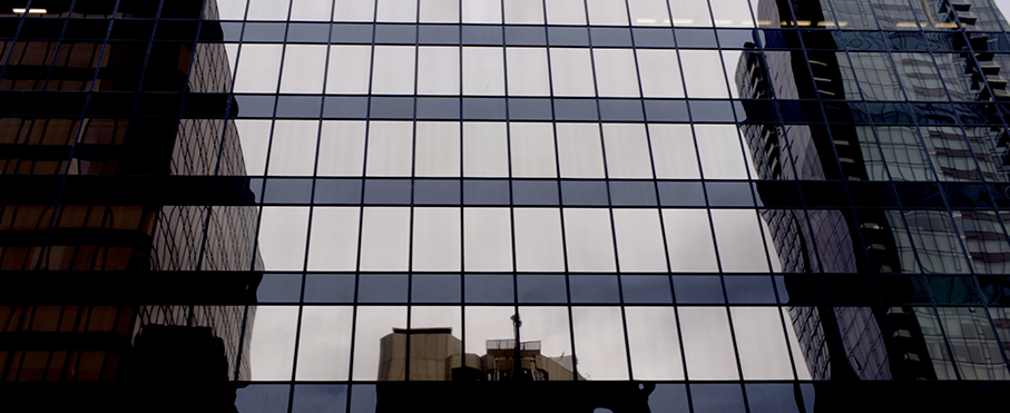 Gros plan sur la façade vitrée d'un immeuble de bureaux moderne, où se reflètent le ciel et les bâtiments environnants.