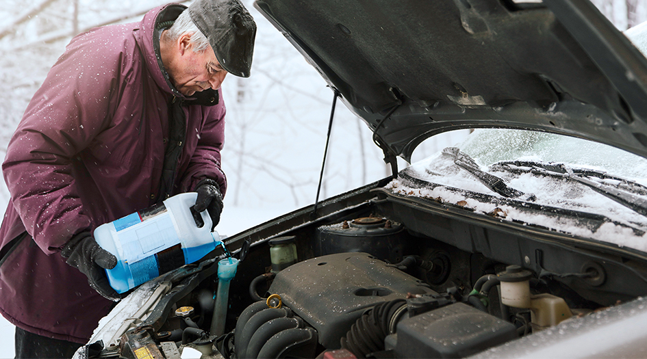 Un homme remplit le réservoir de lave-glace de sa voiture, illustrant comment préparer votre véhicule pour l’hiver