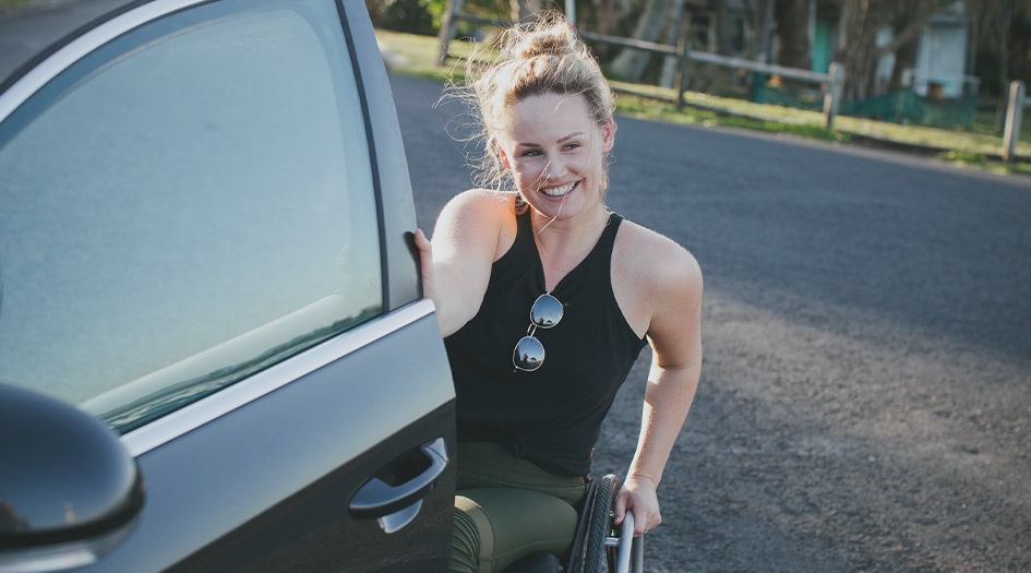 Une femme en fauteuil roulant ouvre la portière de sa voiture, illustrant l’incidence des modifications sur l’assurance auto.