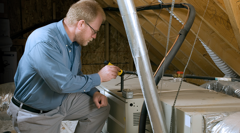 Un homme éclaire une fournaise à l’aide d’un lampe de poche, illustrant comment préparer votre maison pour le printemps.