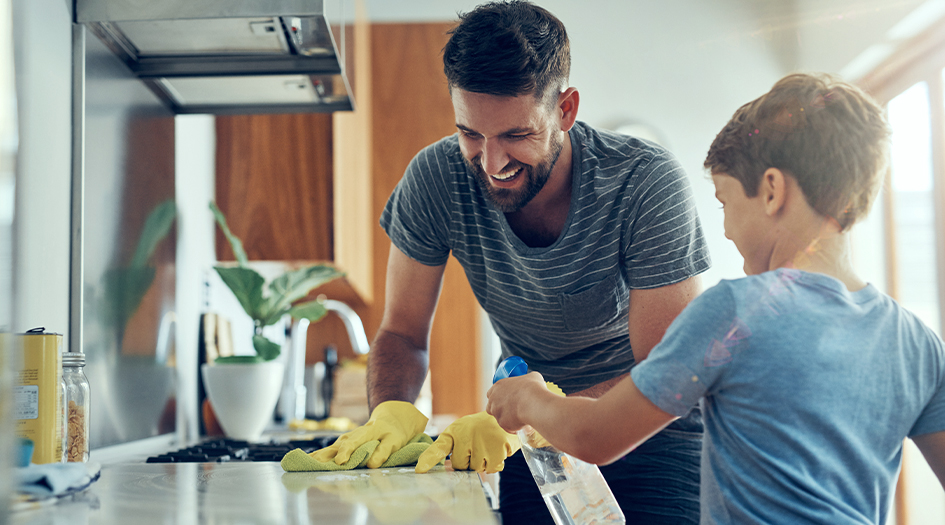 Un homme et un garçon nettoient le comptoir de la cuisine, illustrant quelques conseils pour un ménage de printemps réussi.