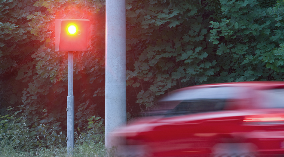 Le clignotant d’un radar routier s’allume parce qu’un véhicule rouge passe devant, démontrant le fonctionnement du radar.