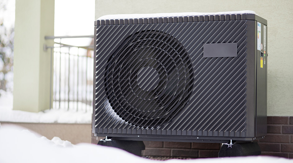 Une thermopompe est fixée sur une maison près d’un sol enneigé pour démontrer les avantages énergétiques de la thermopompe.