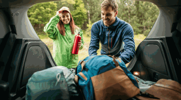 Un homme et une femme placent leurs sacs dans leur voiture, montrant comment préparer un voyage de camping sécuritaire.