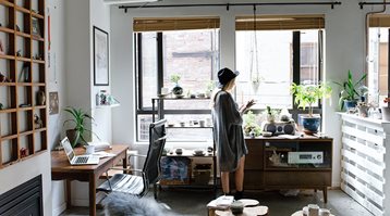 A young woman stands in an open-concept apartment, reading how much tenant insurance costs on her tablet