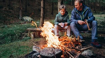 Un homme et un garçon assis sur un banc devant un feu de camp, illustrant quelques manières de prévenir les feux de forêt.