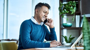A man sits at a desk talking on a mobile phone, as he saves money working with an insurance broker