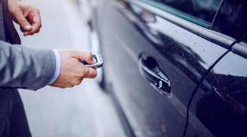 A close up on someone holding their key fob beside their car shows how locking your car can prevent car theft
