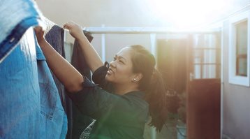 A woman hangs laundry to dry on a clothesline outside, following green cleaning tips for the home and cottage