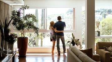 A man and woman look out the window of their living room, showing simple ways to avoid common home insurance claims